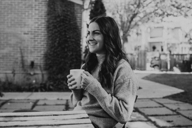 Black and white portrait of young woman sitting outdoors enjoying a cup of coffee.