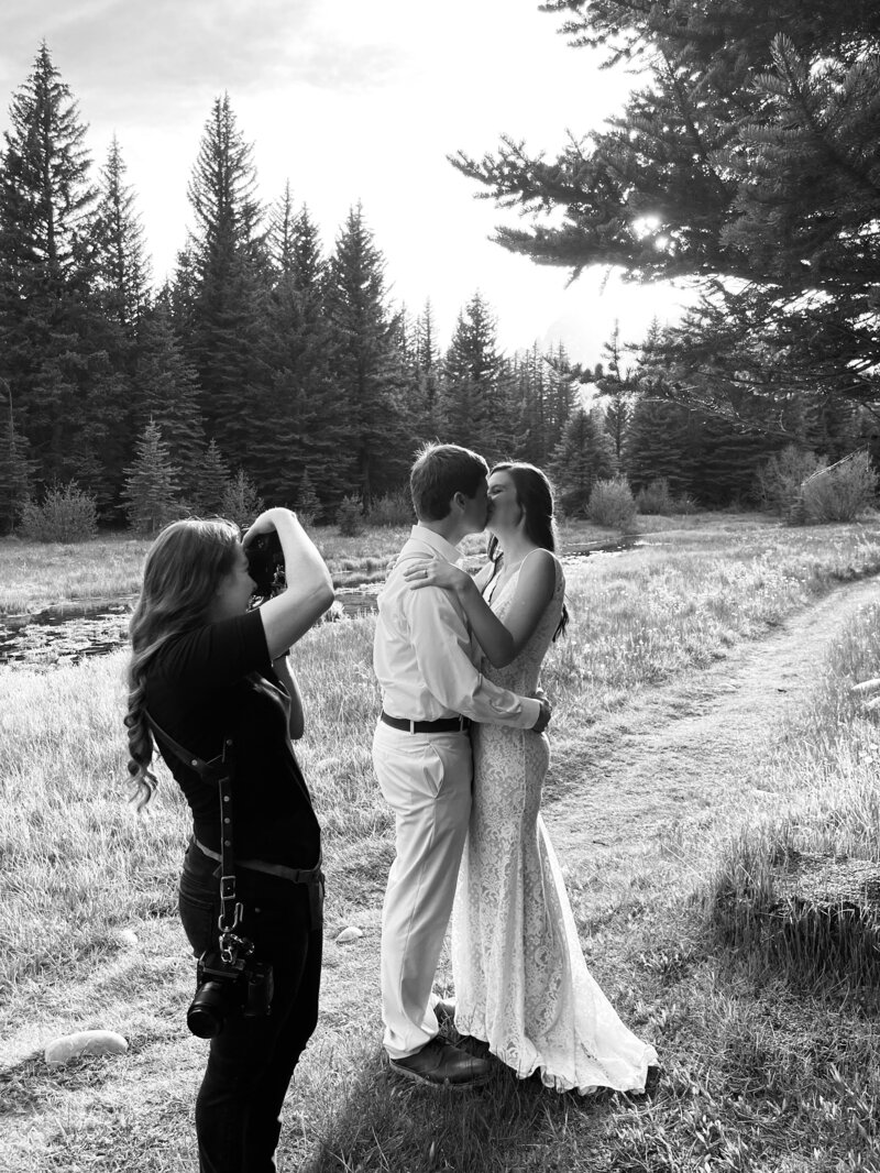 jackson hole wedding photographer working with a couple in the grand tetons with her photographing the bride and groom on a trail in the woods