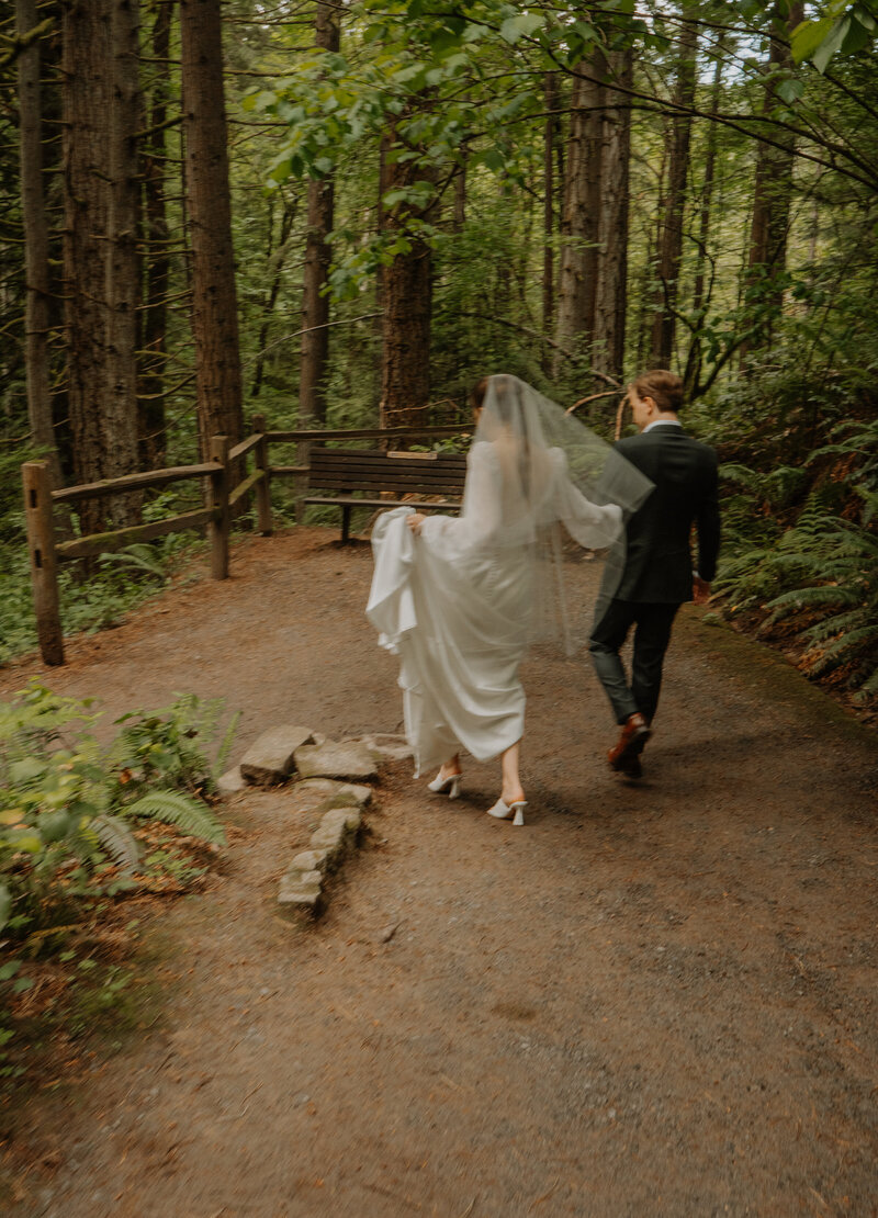Bride and groom holding hands walking down path in a forest