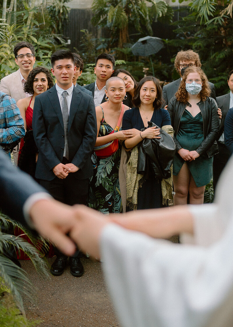 Vancouver wedding photographer captures  friends looking at bride and groom exchange rings during ceremony at Bloedel Conservatory