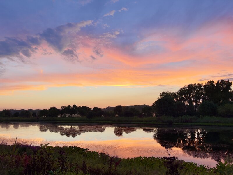 The gradient colors of sunset fade from blue, to purple, to pink; then into orange, then yellow and finally sky blue before reflecting back in reverse on the surface of a pond in Sugar Grove, IL. Fall 2022