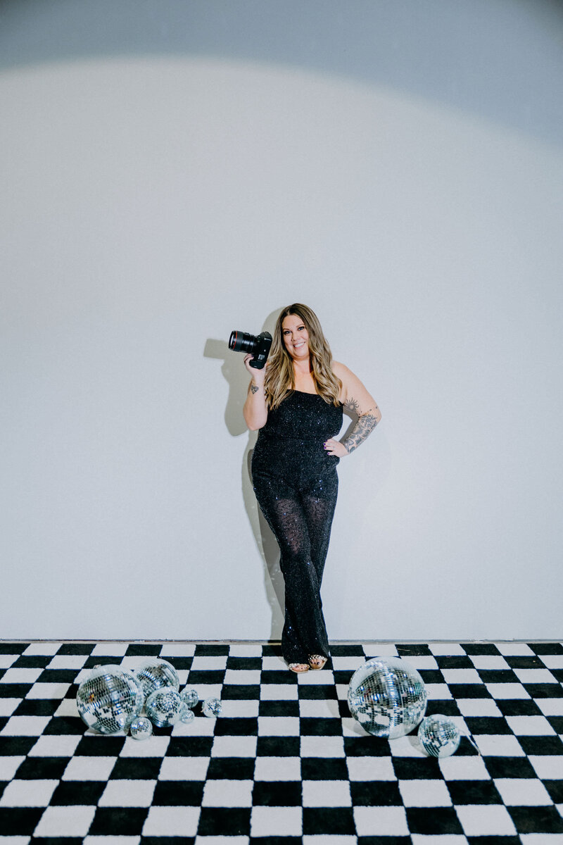 A woman, an Austin wedding photographer, standing on a checkered floor with a camera.