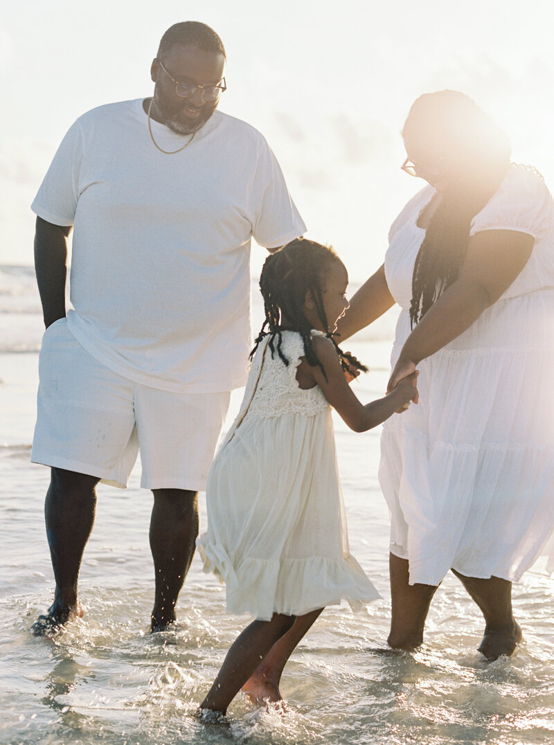 A family dressed in their white, seaside aesthetic dancing in the waves in Rosemary Beach, Florida.