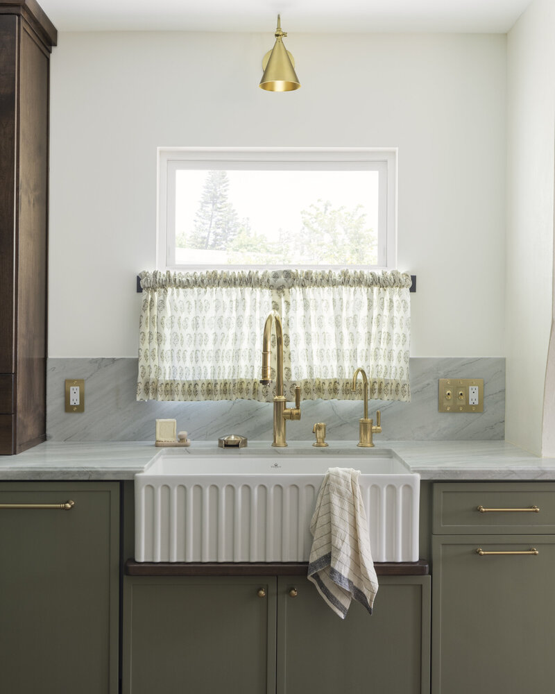 White fluted kitchen sink with  stained drip rail. Quartzite countertops with brass switch plates and brass electrical plates.