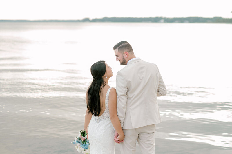 Bride and groom holding hands and looking at each other in front of the Chesapeake Bay  in Kilmarnock, Virginia.