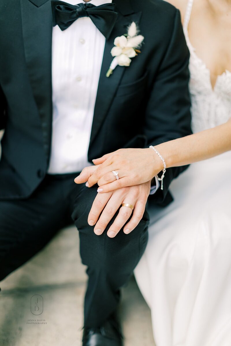 Brides hand on top of grooms hand. Both wedding rings are showing.