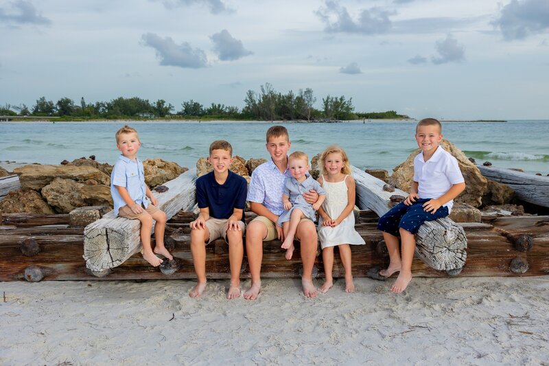 A large group of young siblings and cousins sit together on a jetty.