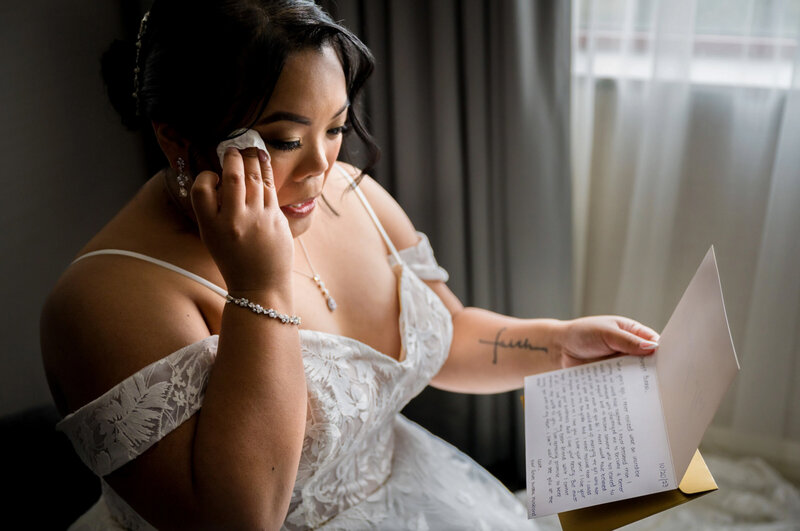 Bride sitting by a window reading a letter from her groom before their wedding at brooklake country club in florham park nj