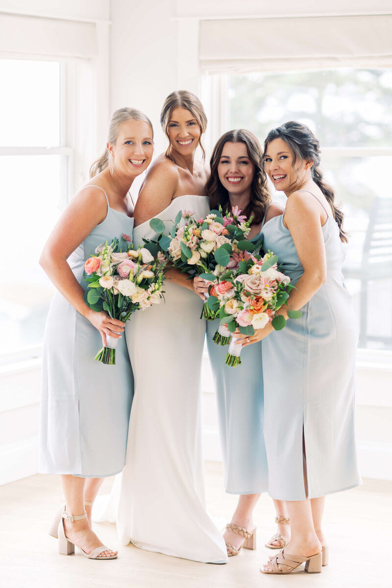 Bride with bridesmaids wearing pale blue dresses and holding colorful florals