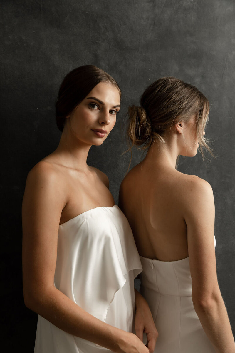 Two brides wearing strapless dresses with loose updos