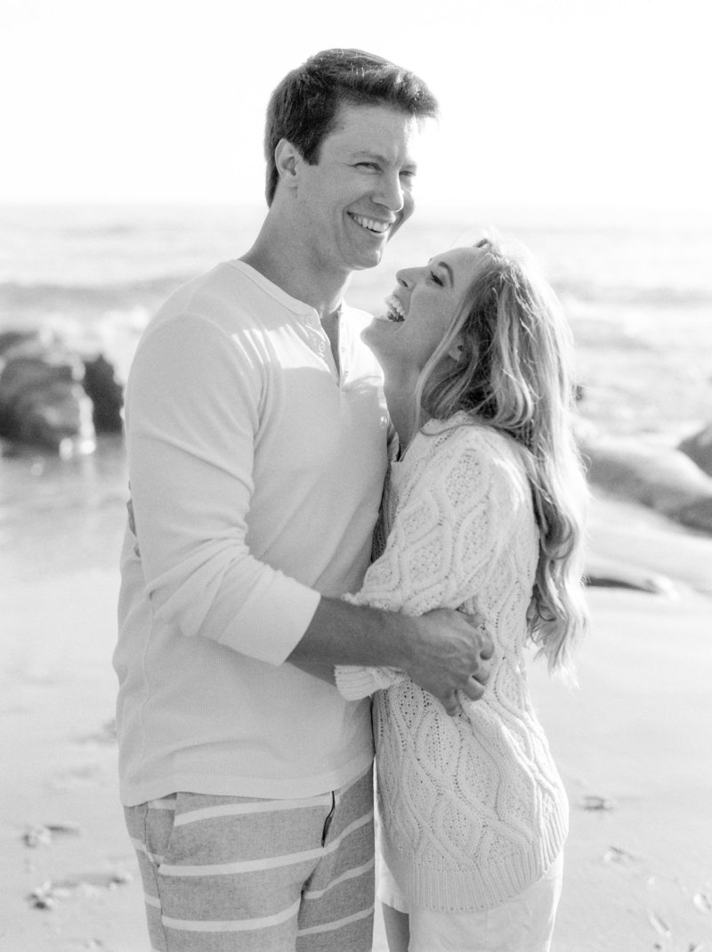 couple laughing close up during engagement session at wind n sea beach. she is wearing a chunky knit sweater