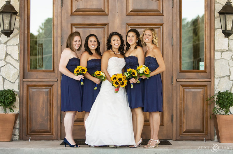 A bride with her bridesmaids photographed in  front of the nice brown wood font doors of Cielo at Castle Pines in Colorado