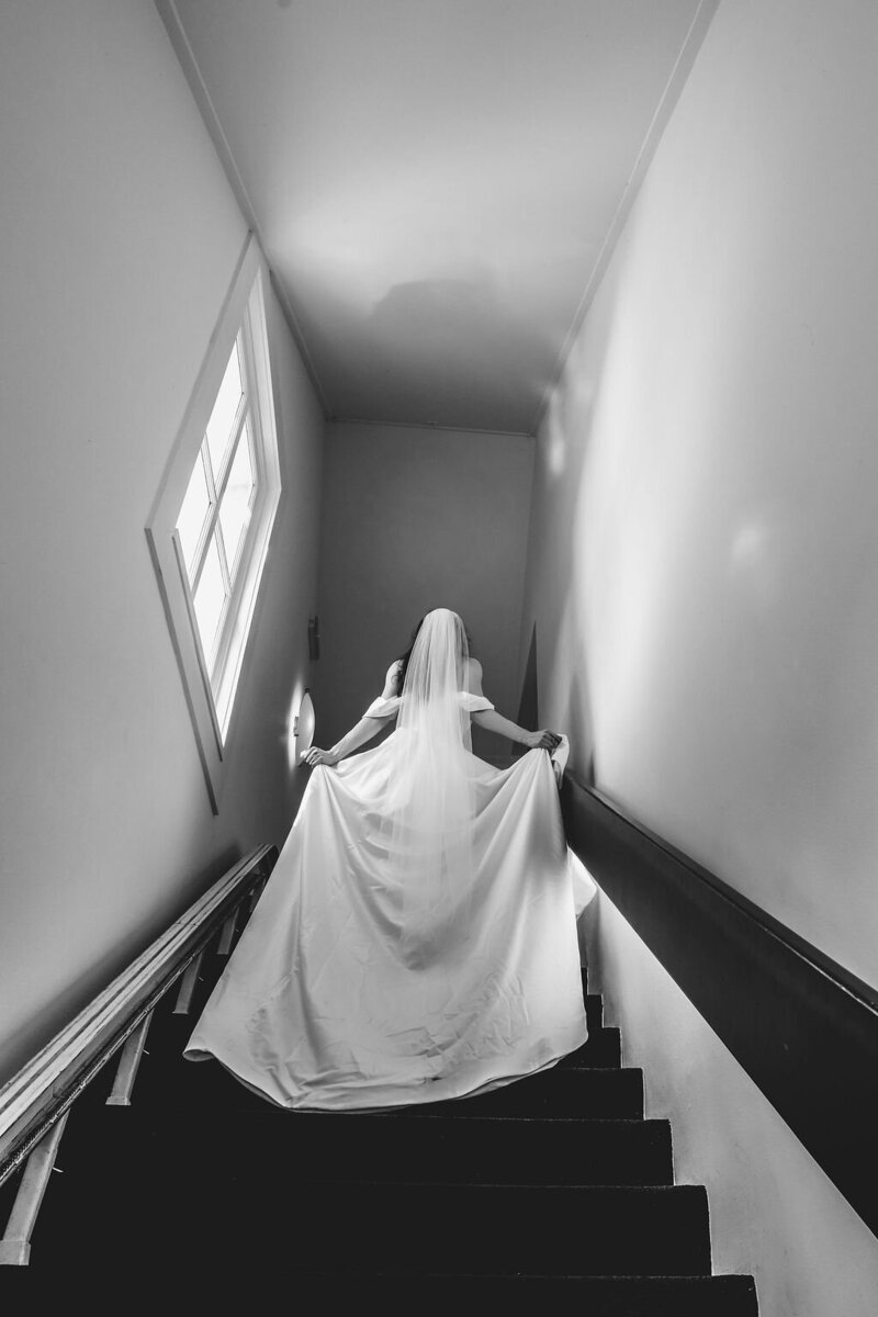 Een stralende bruid loopt de trap op in Oosterbeek, klaar om haar gasten te verwelkomen, begeleid door Timeline Weddings, uw weddingplanner in Gelderland.