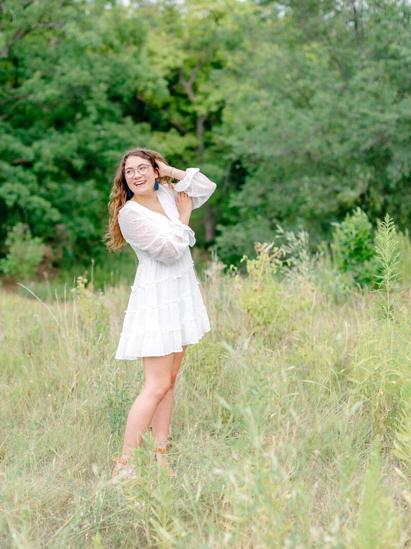 High school senior girl in white dress in a field smiling and playing with her hair