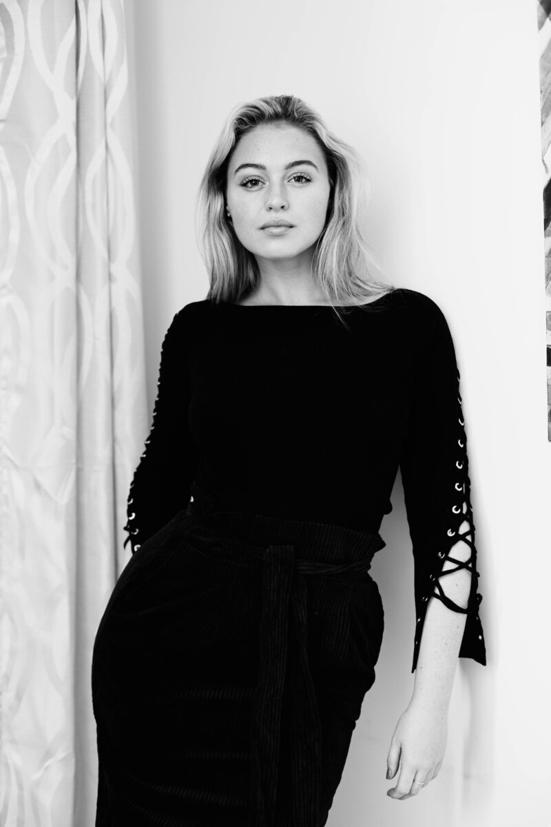 Iskra is posing for the camera in a dark dress.  Photo is black & white.