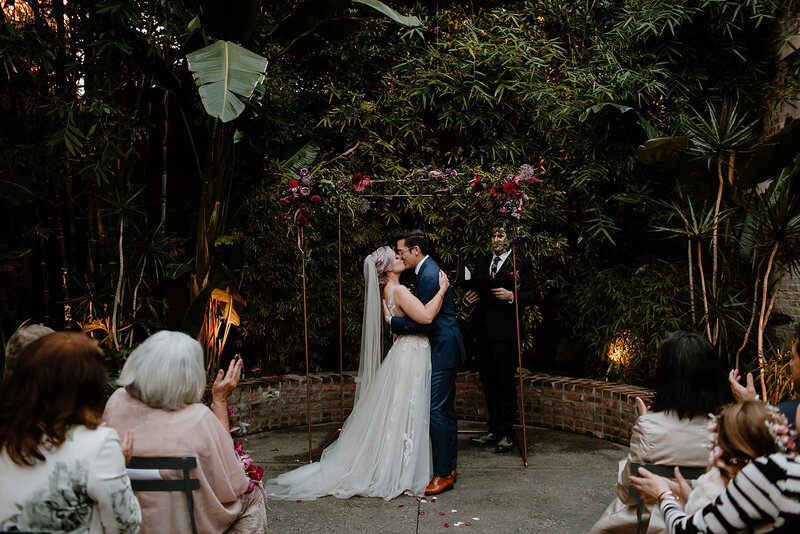 Bride and groom take their first kiss as a married couple in jungle like courtyard ceremony