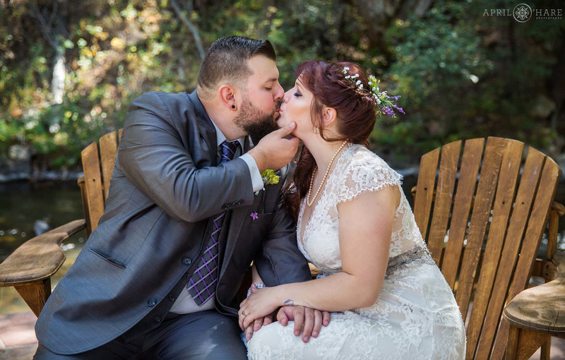 Groom kisses his bride next to Bear Creek at the Bear Creek Cabins in Evergreen Colorado