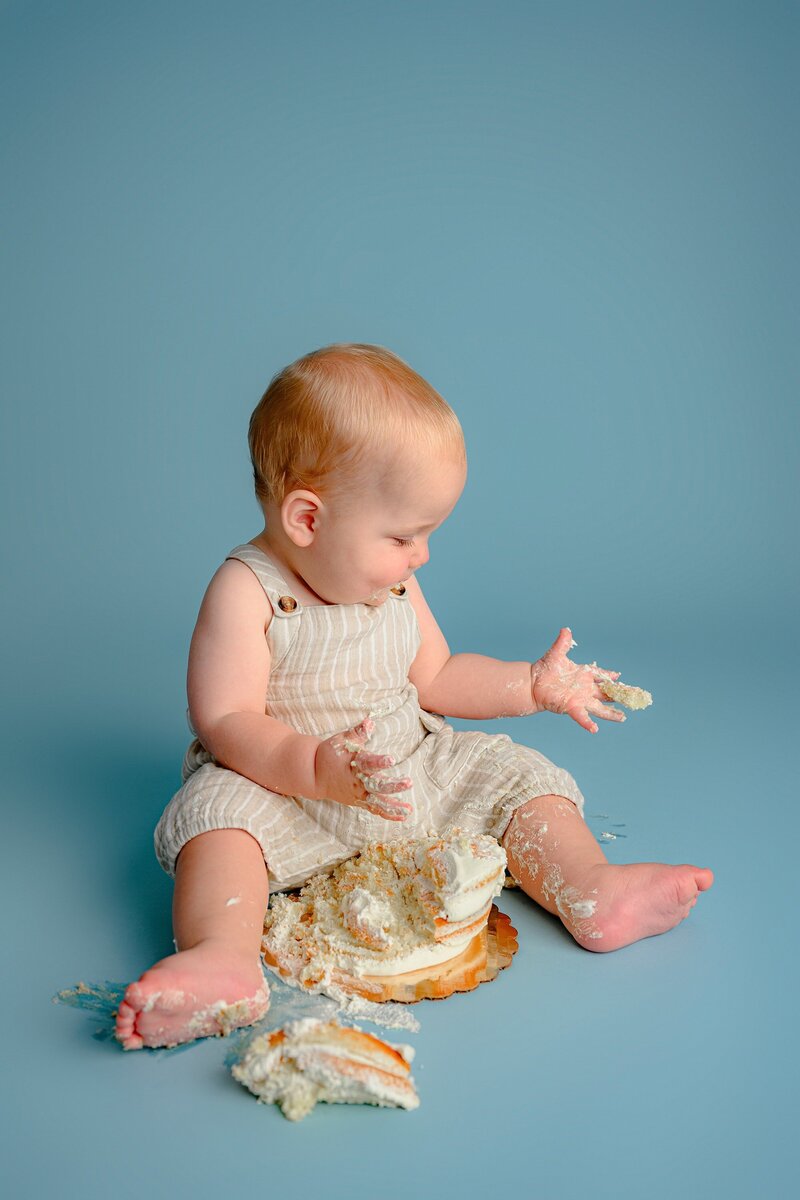little boy looks at his hand covered in cake