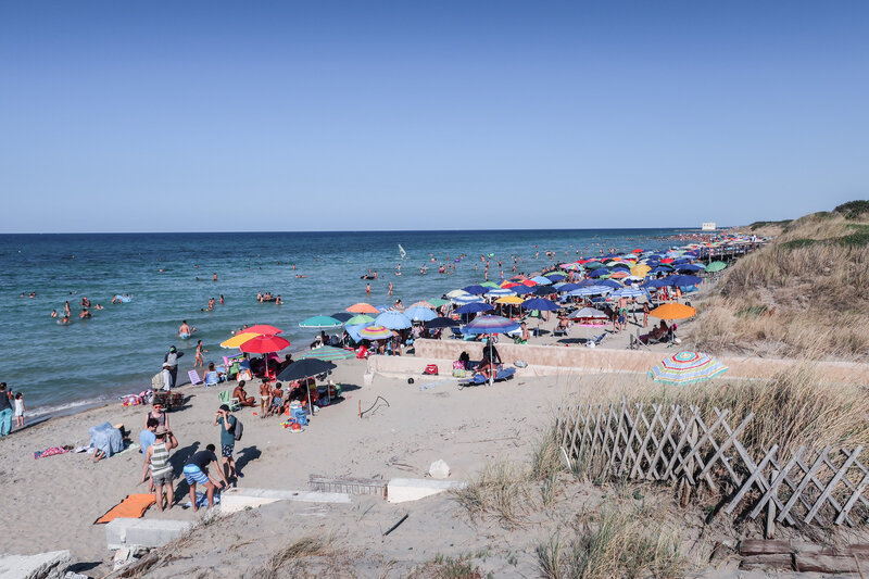 Dozens of brightly colored umbrellas with beach goers beneath them on the beach in Sicily