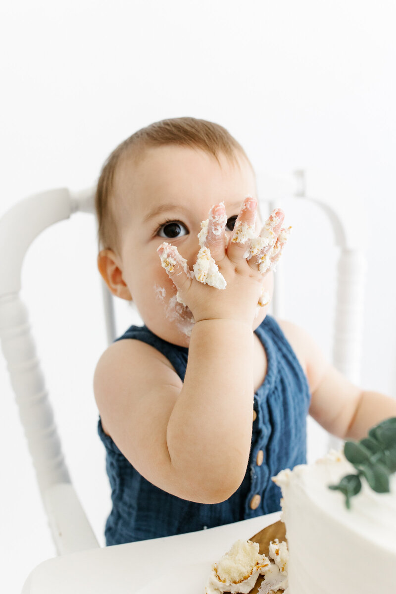 One year old boy licking cake off his hand