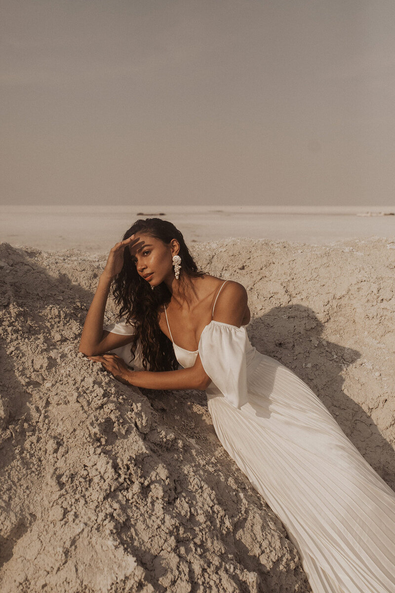A woman in an elegant white dress posing in a barren landscape.
