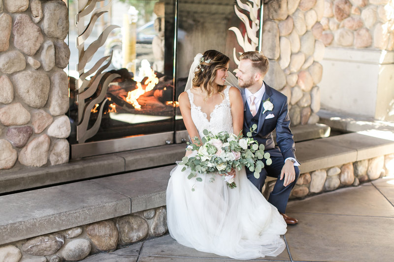 Bride and groom looking at each other sitting in front of stone fireplace