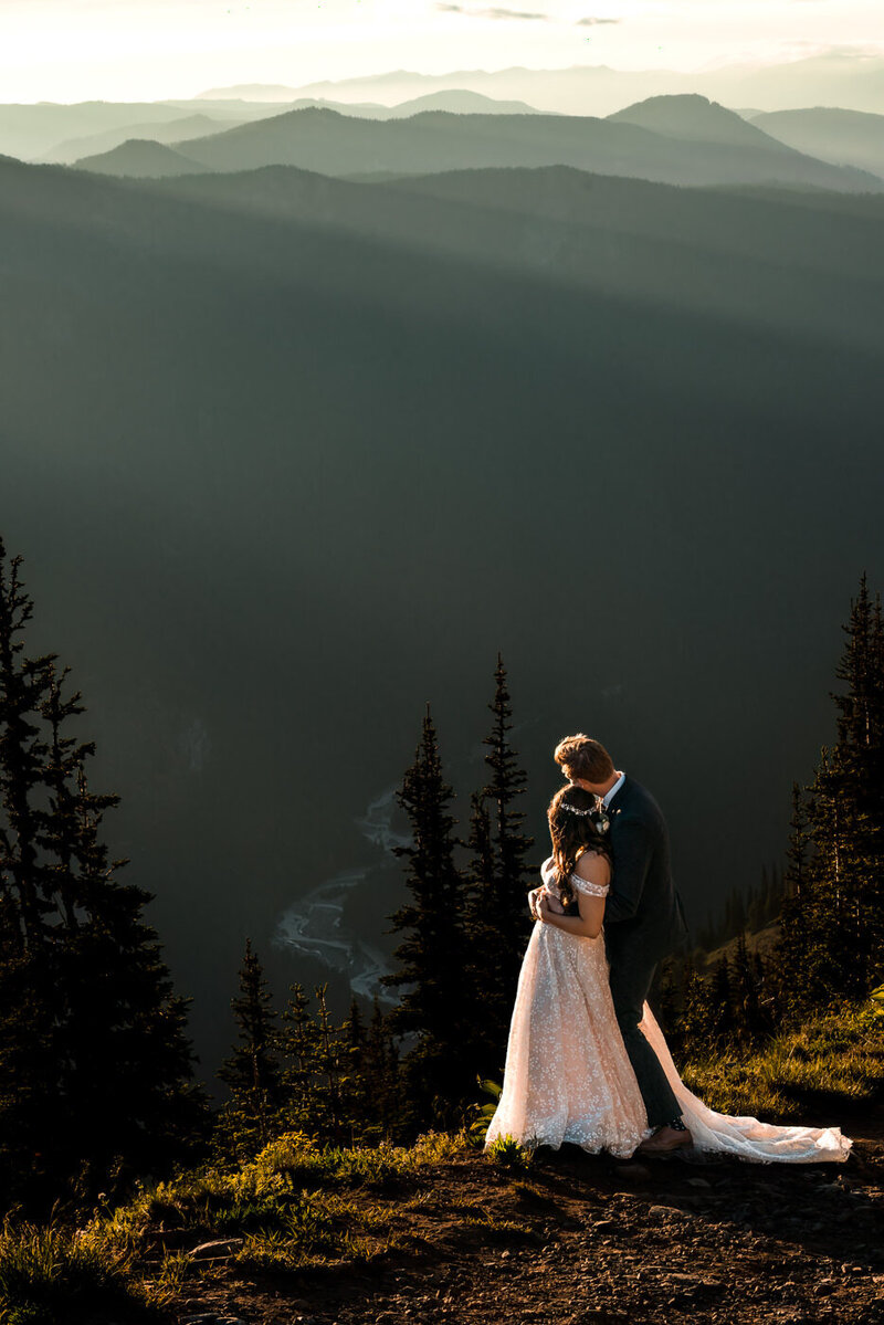 A couple gazes out towards the mountains in their wedding attire, during sunset on their olympic national park wedding