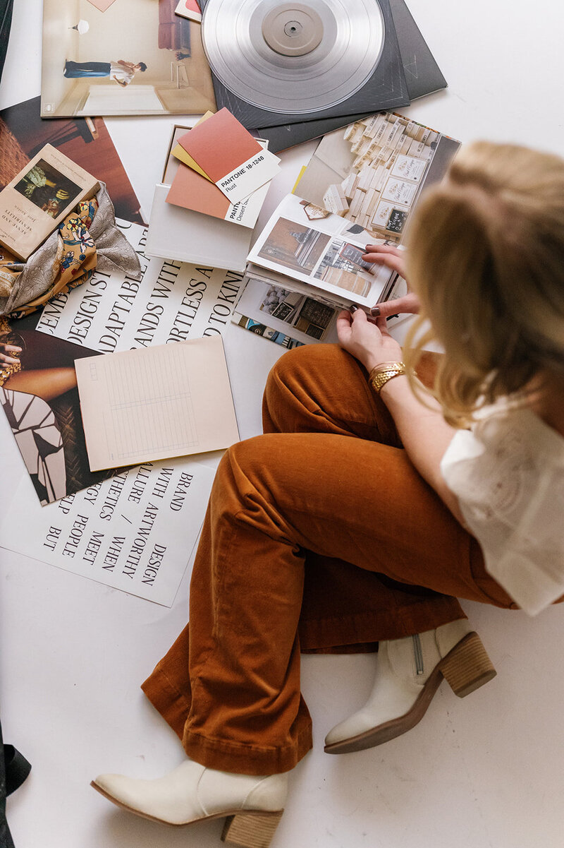 Woman in orange pants sorting through paper and pictures on the floor