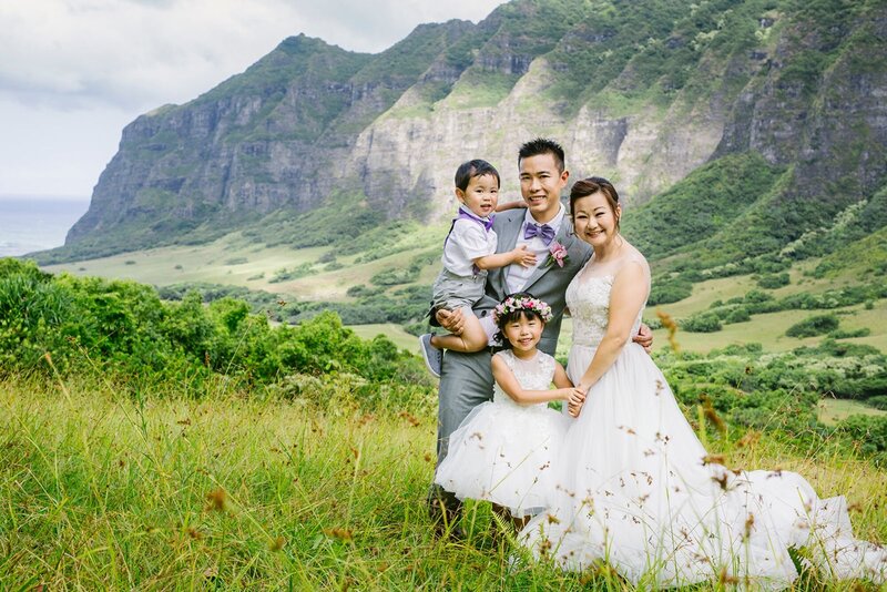 A woman wearing a wedding dress with her husband and two children pose for a photo at Kualoa Ranch.