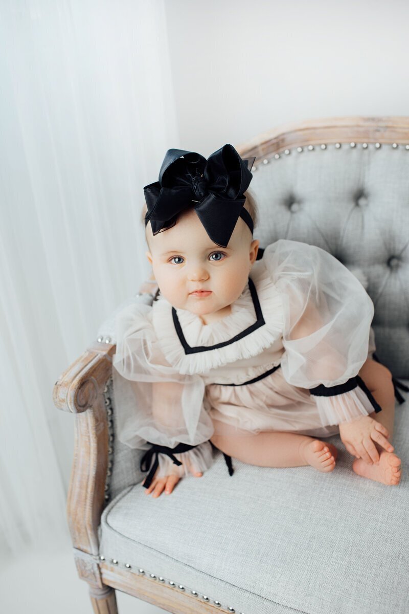 Baby with black bow and dress sitting on bench taken by baby photographer nj