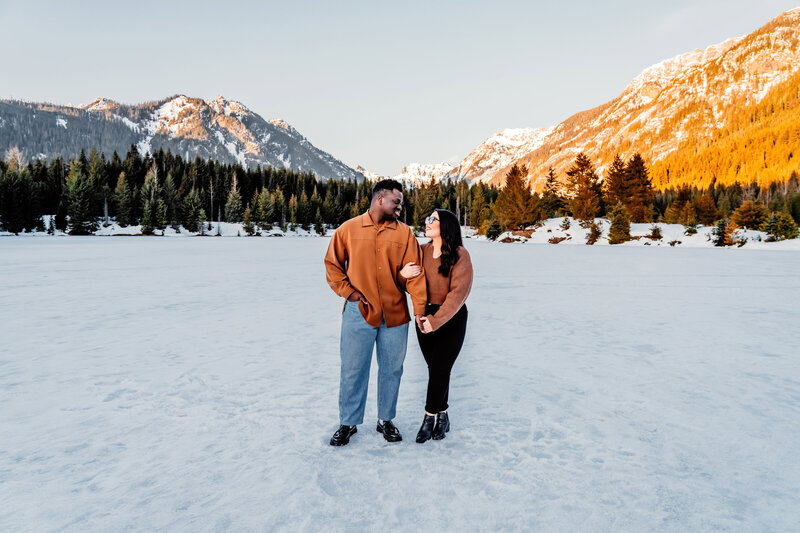 a POC couple standing  in front  of a washington mountain range during sunset