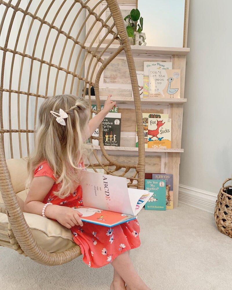 Young girl sits cozy in  reading nook with bookshelf and hanging chair