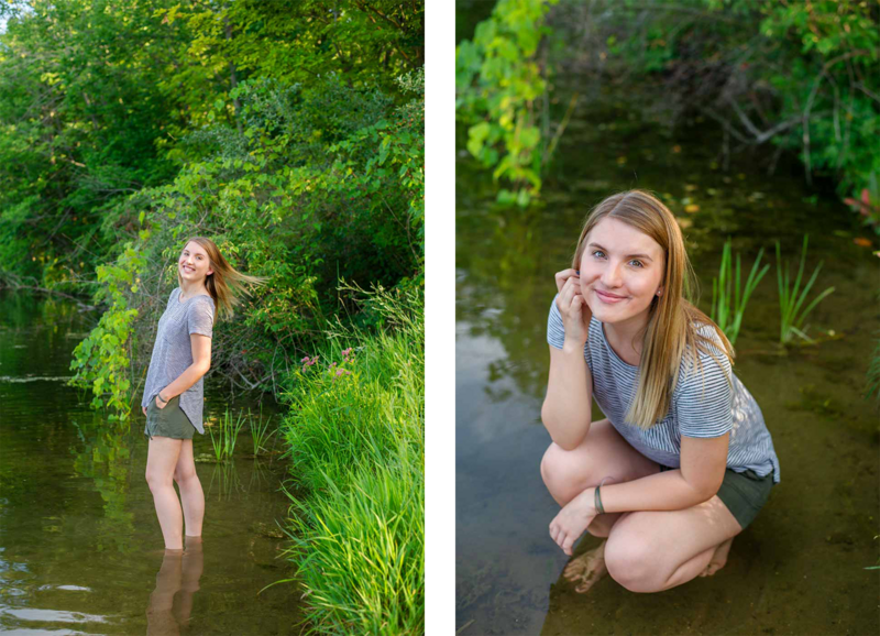 high school senior girl posed in shallow end of water at a lake with green trees  around her
