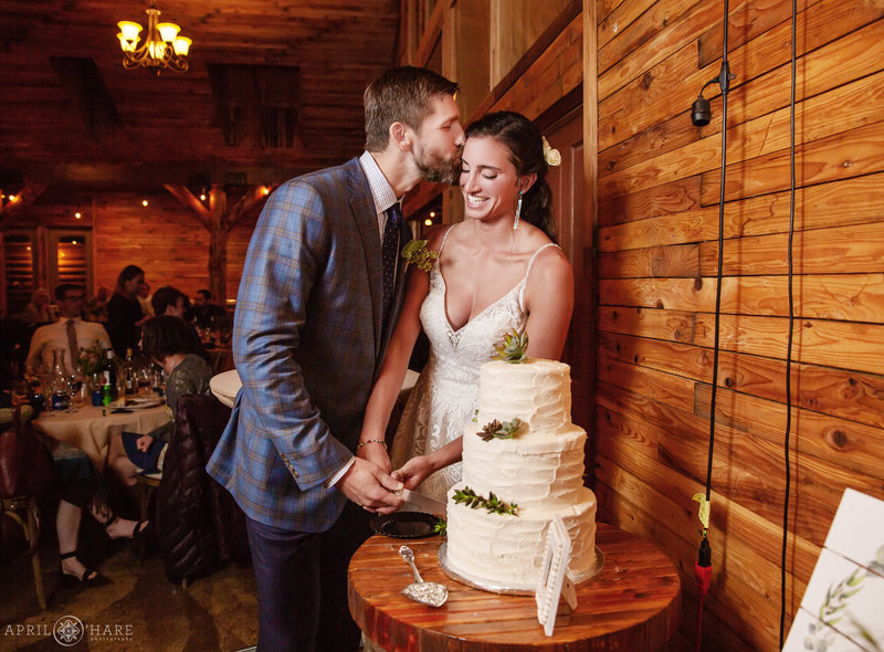 Cute couple kisses as they cut their wedding cake at Mountain View Ranch Wedding Reception in the Barn
