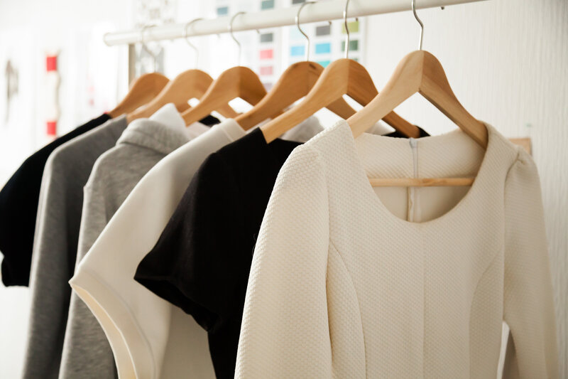 A collection of black, white and gray blouses on  wooden hangers