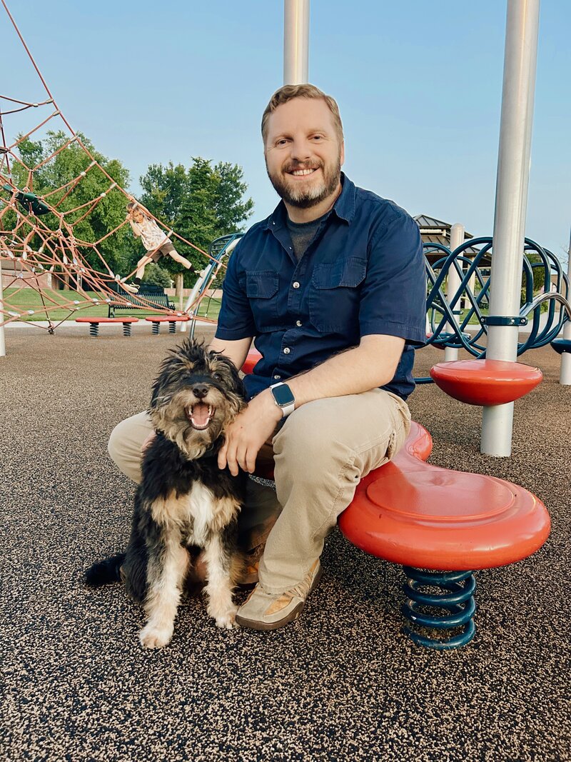 Jason sits on playground equipment with dog in a sit next to him