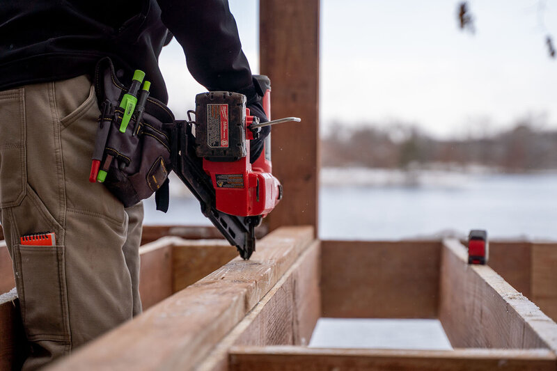 Deck builder using a nail gun on a KDAT deck frame during a Minnesota winter. 