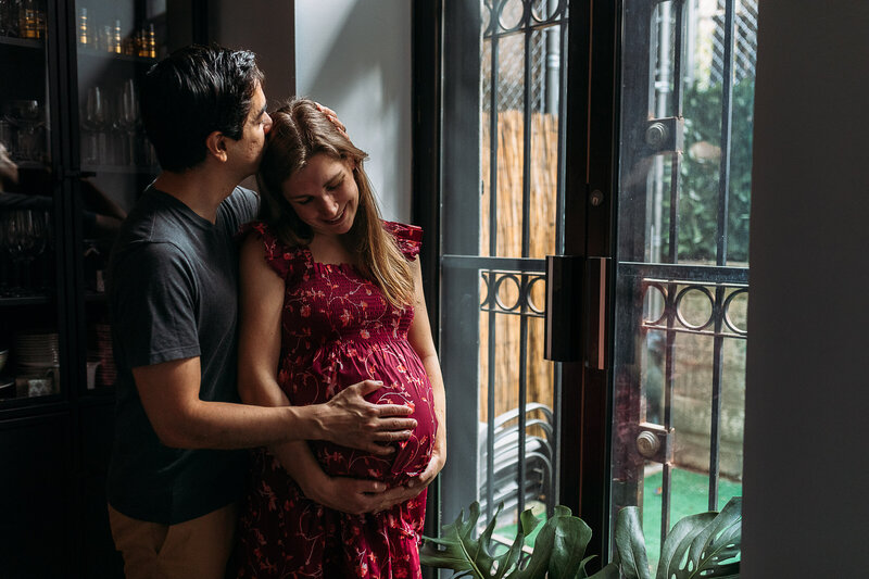 Maternity Photographer, a husband kisses his pregnant wife near a window sill