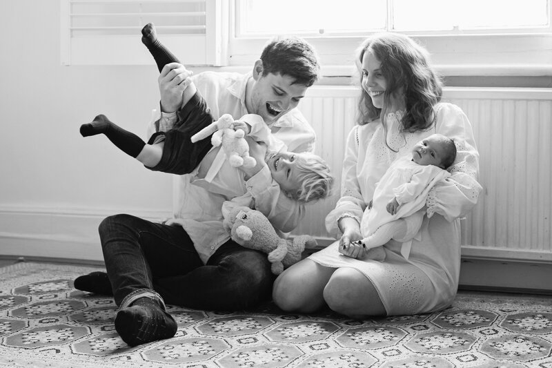 Photograph of newborn and her older brother playing at home with parents