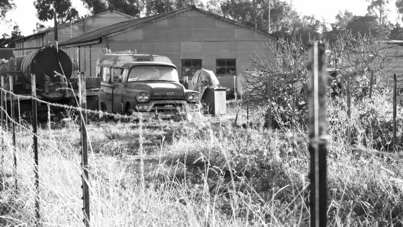 Black and white photo of vintage GMC truck and old metal farm building