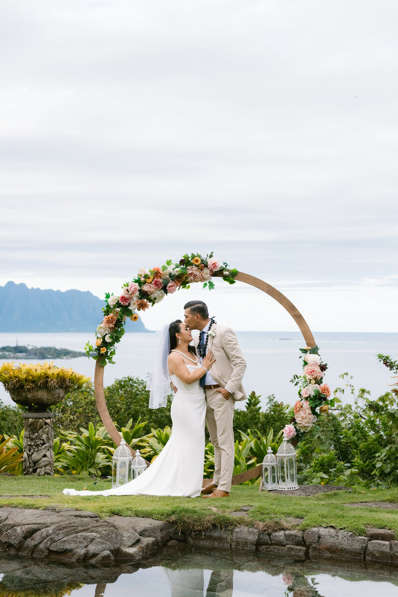 A newlywed couple shares a heartfelt kiss just moments after saying "yes" during their intimate elopement in a private garden in Oahu