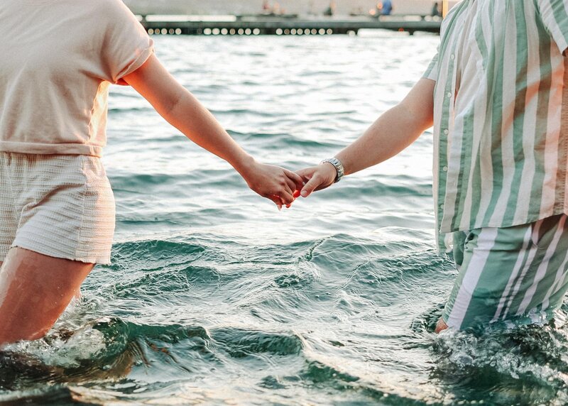A couple hold hands while playfully in the water.