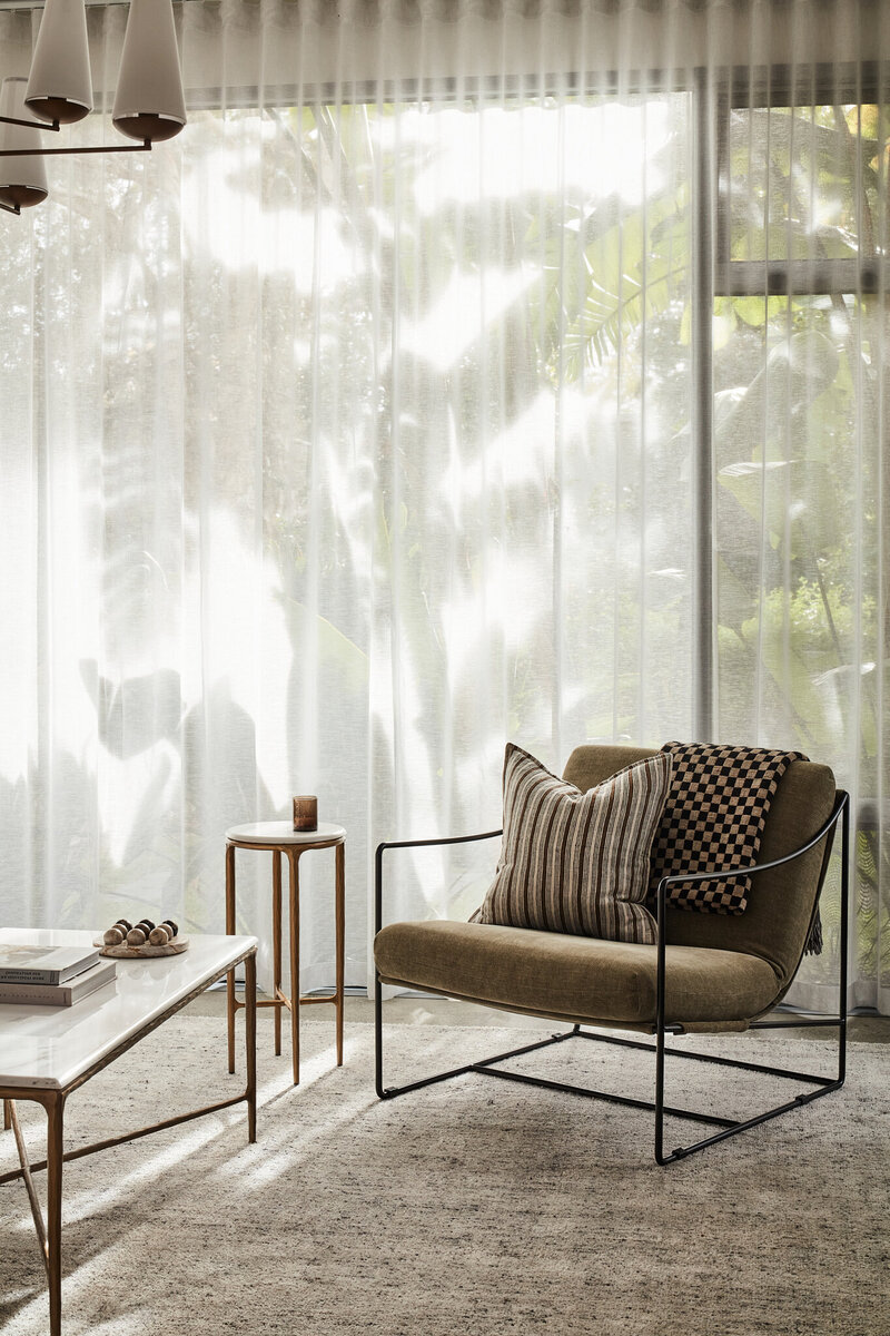 Contemporary lounge chair with striped cushion beside tall sheer curtains, styled with nesting side tables.