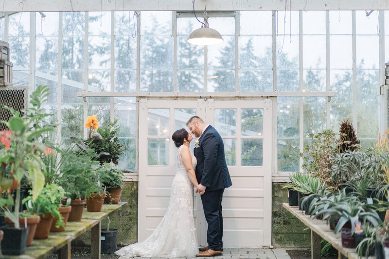 bride and groom face each other and kiss in a greenhouse at christianson's farm