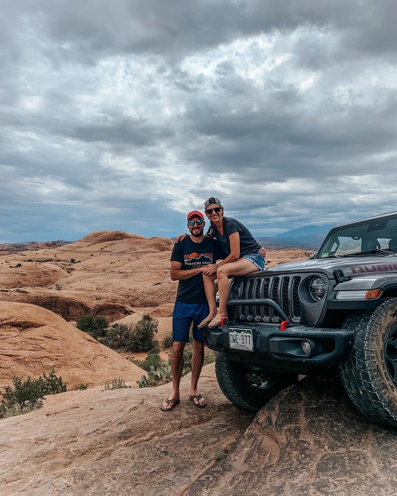 husband and wife sitting on hood of jeep
