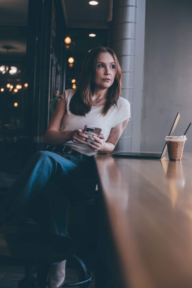 A person stands against a wall, wearing a black blazer over a black top, distressed jeans, and a baseball cap. Their arms are relaxed by their sides, and they are barefoot—embodying the casual yet confident look of a web designer for small business projects.