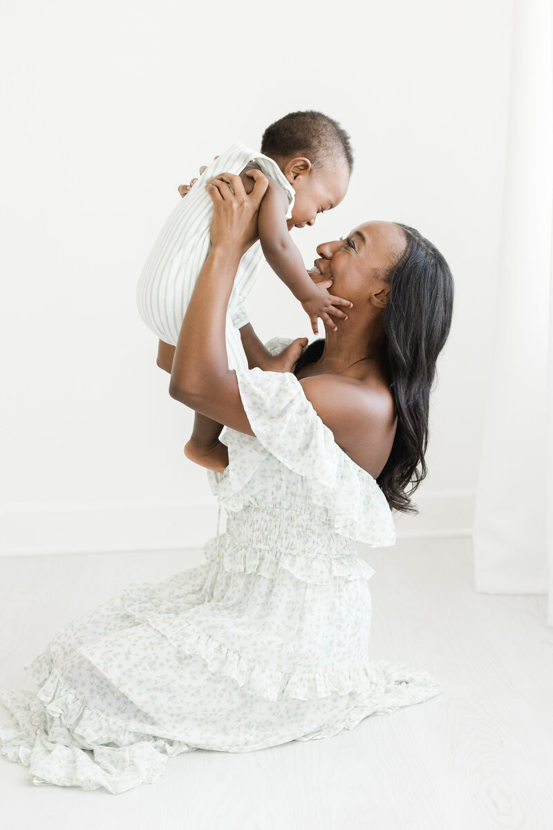 Mother raises her 6 month old baby in the air during baby milestone portrait session