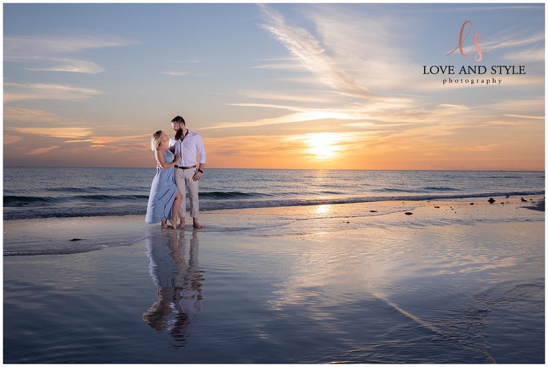 gorgeous engaged couple standing on Siesta Key Beach with their reflection in  the water and sun setting behind them