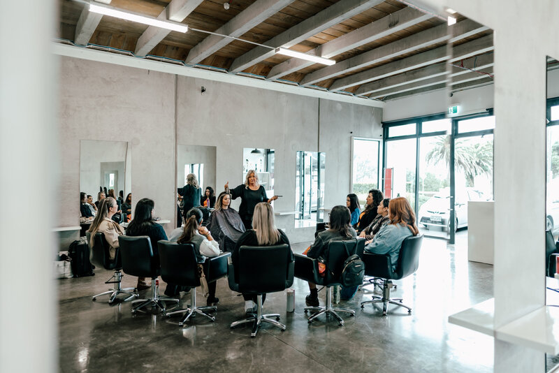 A group of hair and make-up stylists sitting during a live training with a head hair stylist capture by Zanthe Vorsatz Photography