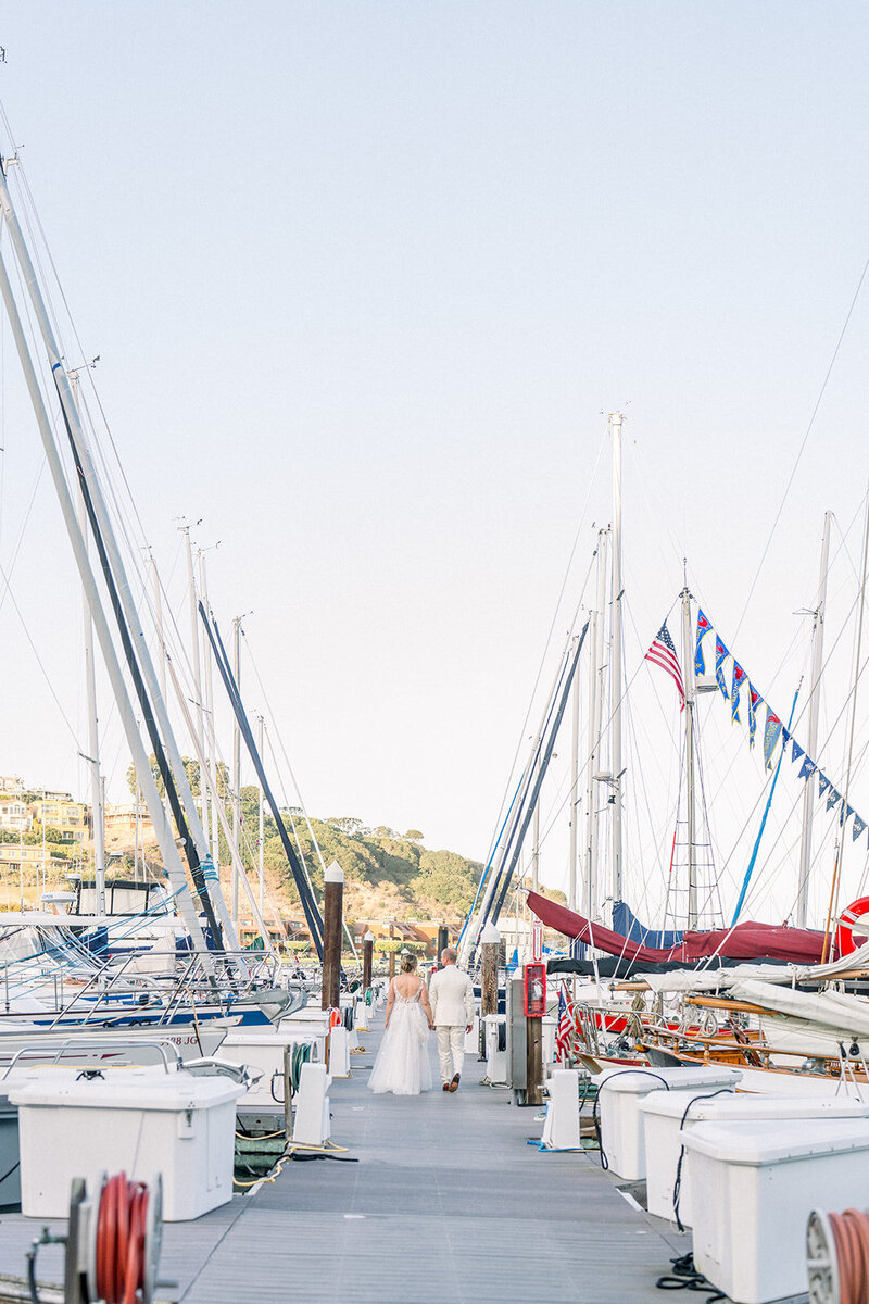 Guests walk down the sailboat dock at a Tiburon marina wedding in the San Francisco Bay Area captured with a documentary approach.